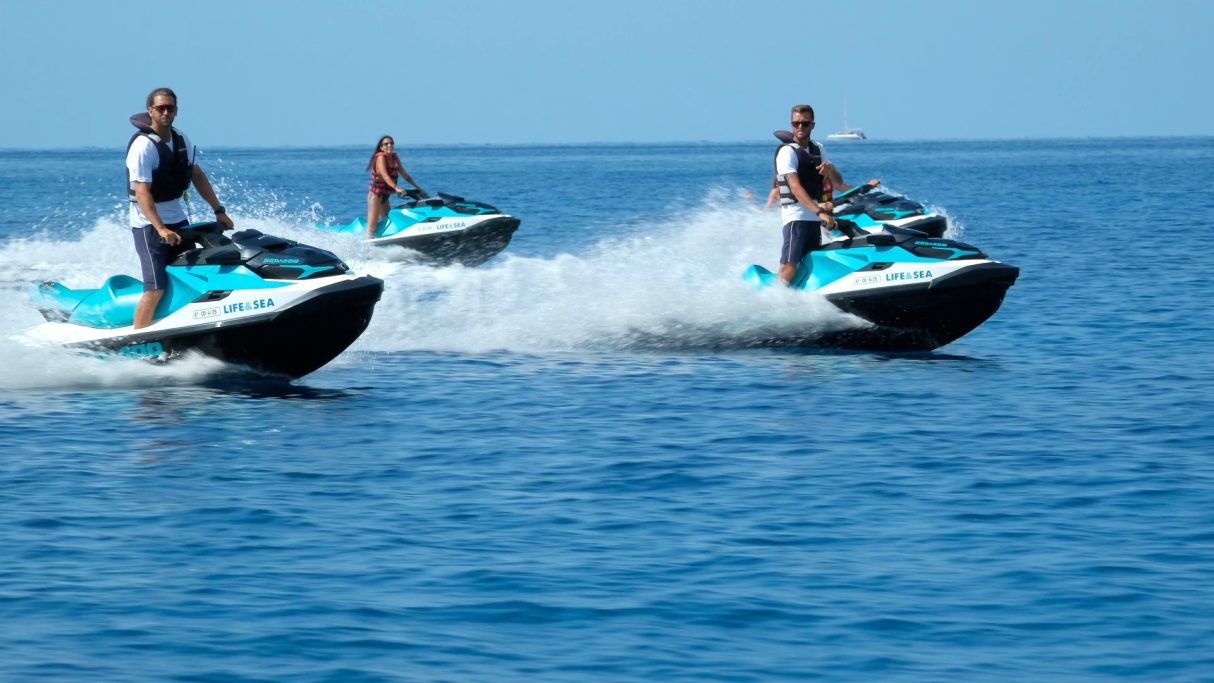 Cuatro personas montando motos de agua sobre un océano azul claro.