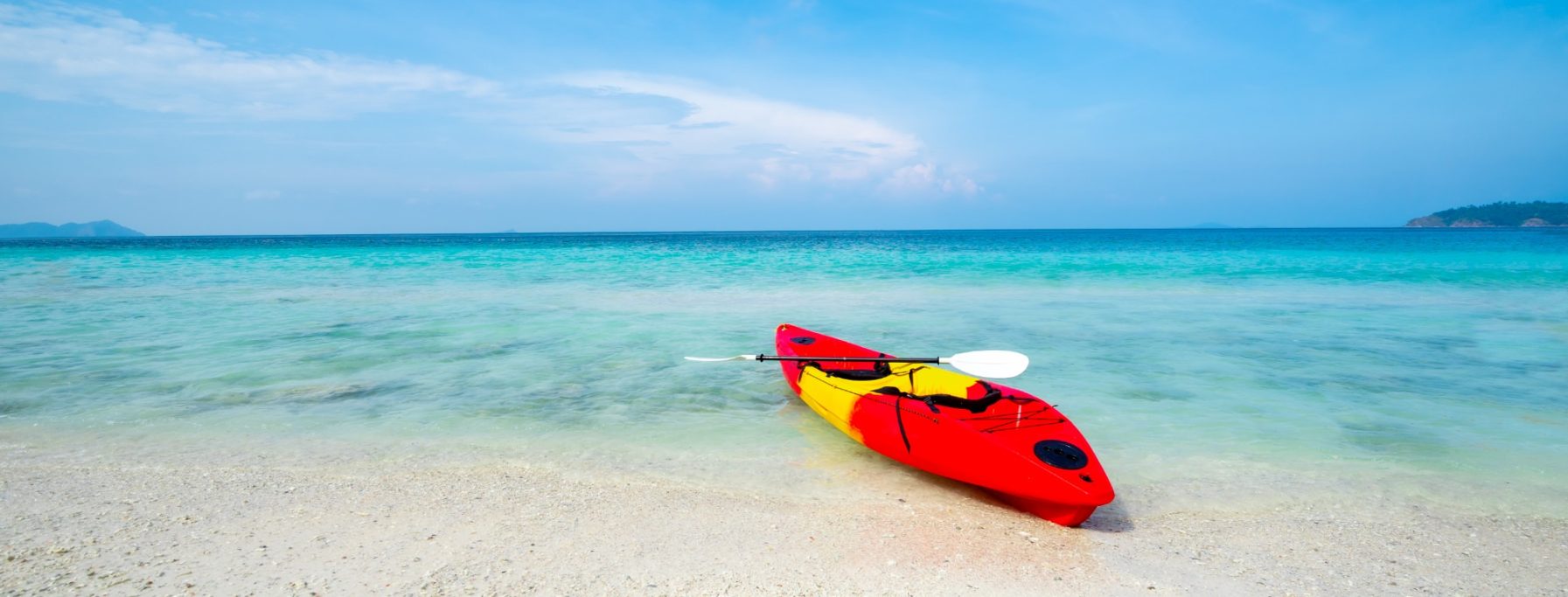 Kayak rojo en una playa de arena, junto a aguas azul claro y cielo despejado.