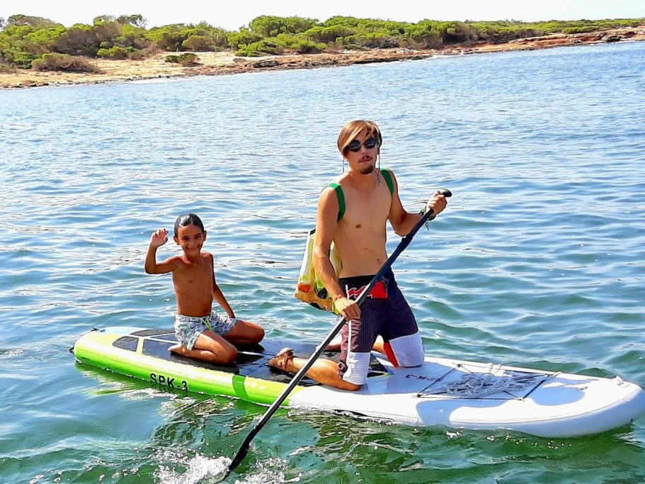 Dos niños hacen paddle surf en un cuerpo de agua, disfrutando de un día soleado.