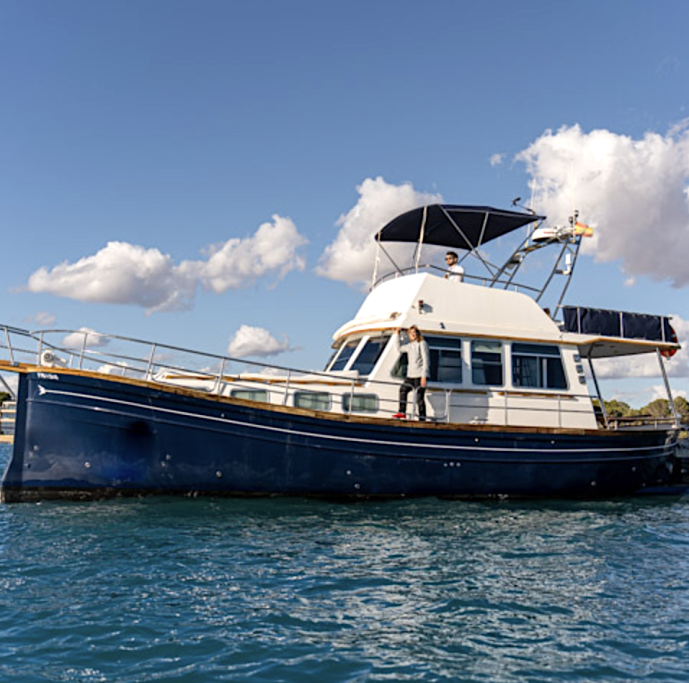 Yate de motor anclado en un puerto, con nubes y cielo despejado de fondo.