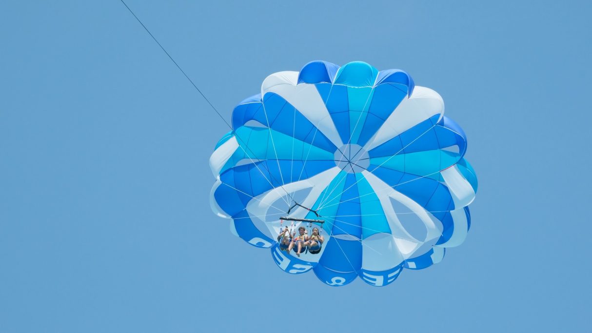Persona volando en paracaídas sobre un fondo azul, con un paracaídas azul y blanco.