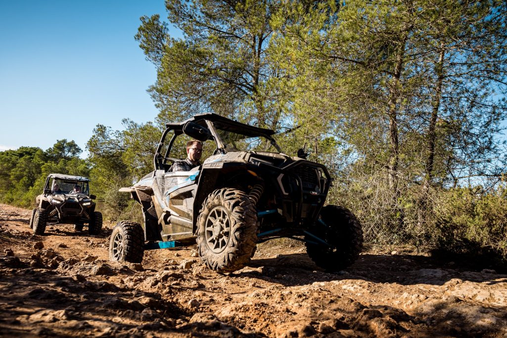 Vehículos todoterreno circulando por un sendero de tierra entre árboles.