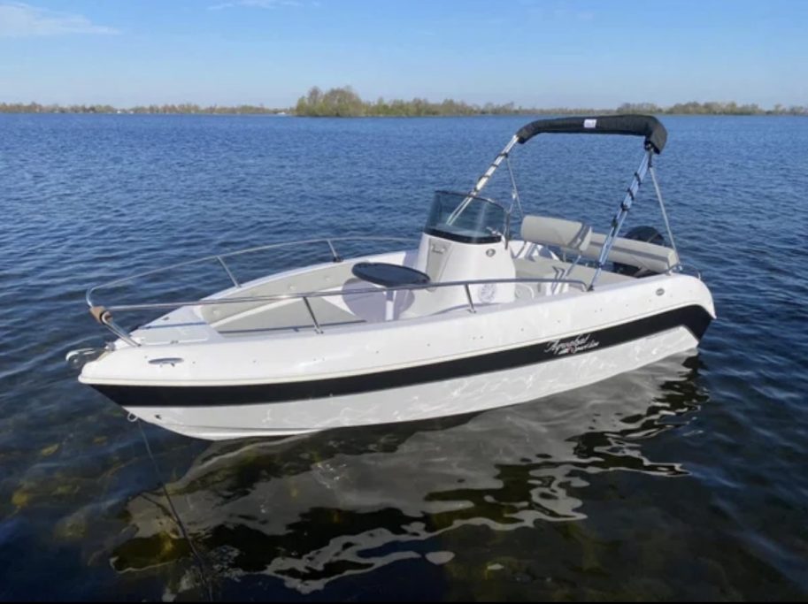 Barco blanco con detalles negros anclado en el mar, con cielo azul y un día soleado
